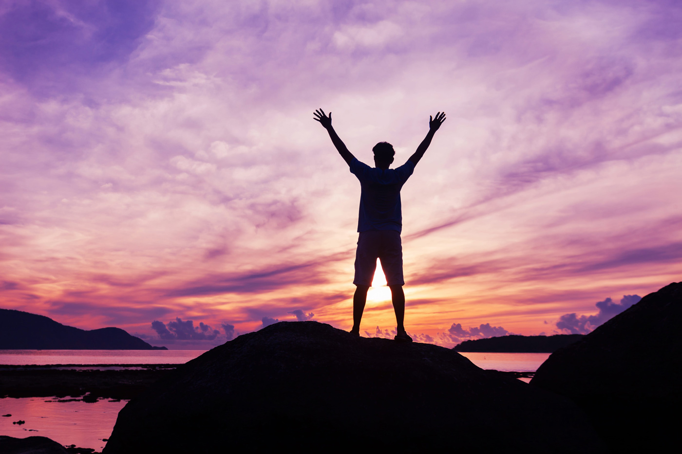 The silhouette of a man with his arms in the air is proud of his success in front of a lovely purple and blue cloudy sky in the background.